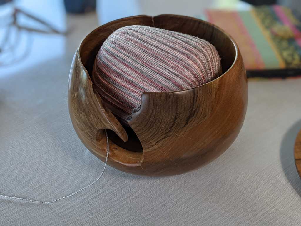 A yarn bowl with a ball of yarn in it, trailing out of a slot carved into the side of the bowl